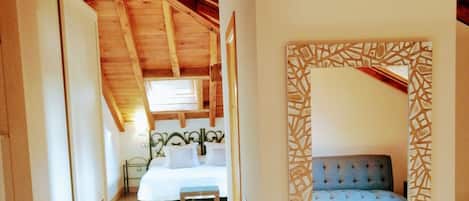 A narrow hallway leading to a bedroom with a bed, bedside table, and a blue sofa.