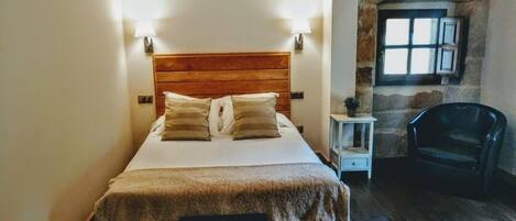 A neatly made bed with a wooden headboard, two bedside lamps, and a stone wall with a window.