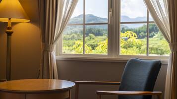 Une pièce avec une fenêtre donnant sur un paysage montagneux, comprenant une chaise, une table et une lampe.