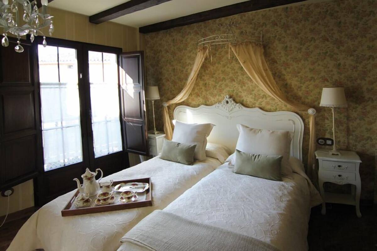 A double bed with a canopy, a tray with tea set, and a nightstand with a lamp.