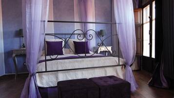 Un dormitorio con cama con dosel, una mesita de noche, una lámpara y una ventana con cortinas.