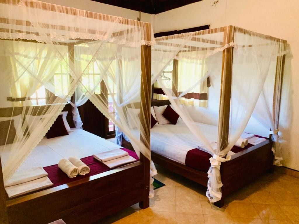 Two single beds with white canopies, each with a wooden frame and a red pillow.