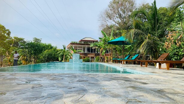 Una piscina con cascada, rodeada de tumbonas y palmeras.