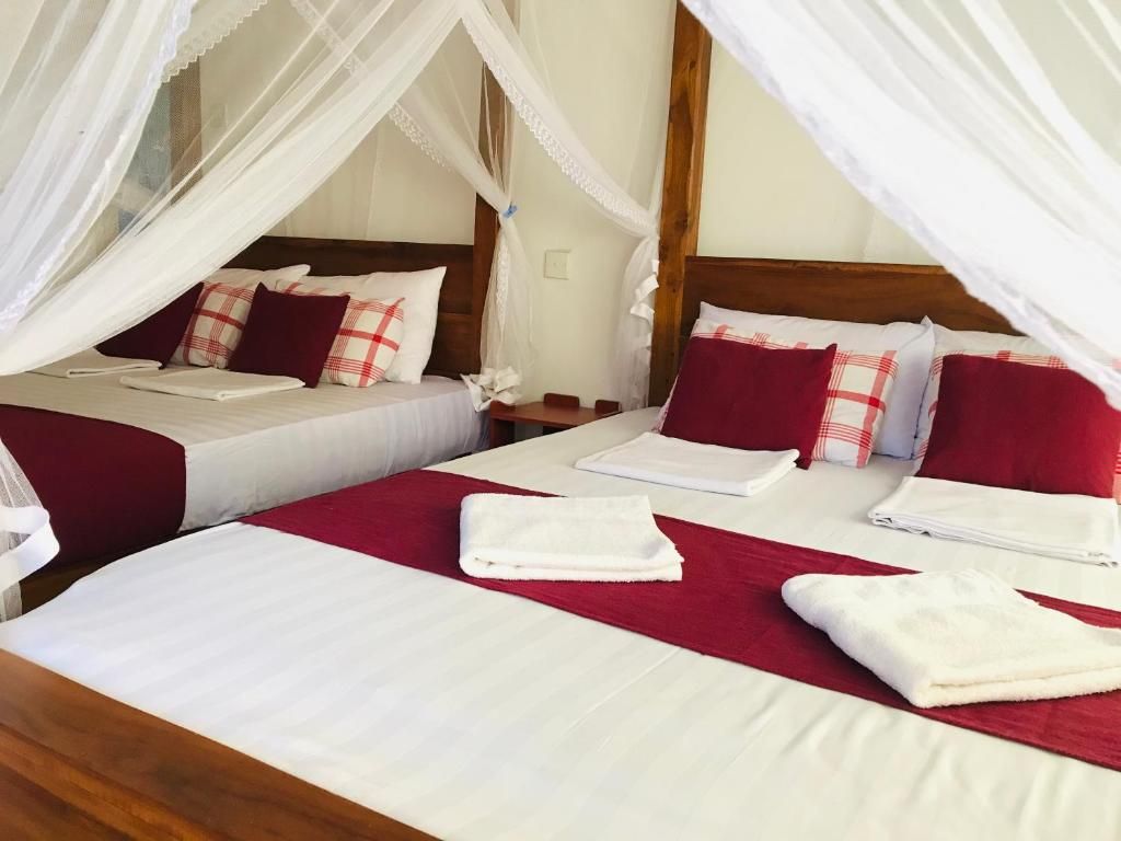 Habitación de hotel con dos camas, cada una con ropa de cama blanca y detalles rojos, y una cama con dosel y ropa de cama blanca.