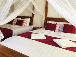 Habitación de hotel con dos camas, cada una con ropa de cama blanca y detalles rojos, y una cama con dosel y ropa de cama blanca.