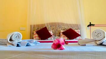 Un letto rifatto con una coperta bianca, due asciugamani arrotolati, un fiore rosa e una tenda a baldacchino.