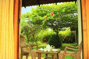 Un área de estar al aire libre con una mesa preparada para tomar té, rodeada de follaje y árboles.