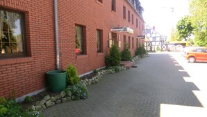 Een gebouw van rode bakstenen met een geplaveid pad, een groene prullenbak en een rij geparkeerde auto's.