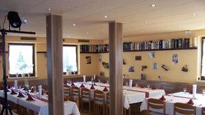 Een restaurant met meerdere tafels voor diners, houten vloeren en een boekenkast met diverse objecten aan de muur.