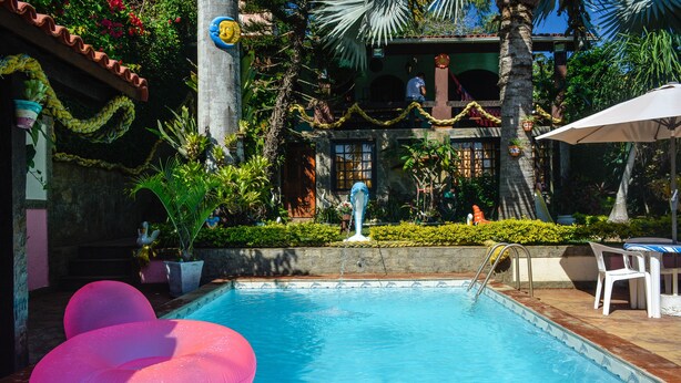 A swimming pool with pink inflatable loungers, surrounded by lush greenery and a tiled deck. - Suites Casa do Barão (Búzios)