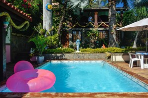 A swimming pool with pink inflatable loungers, surrounded by lush greenery and a tiled deck. - Suites Casa do Barão (Búzios)