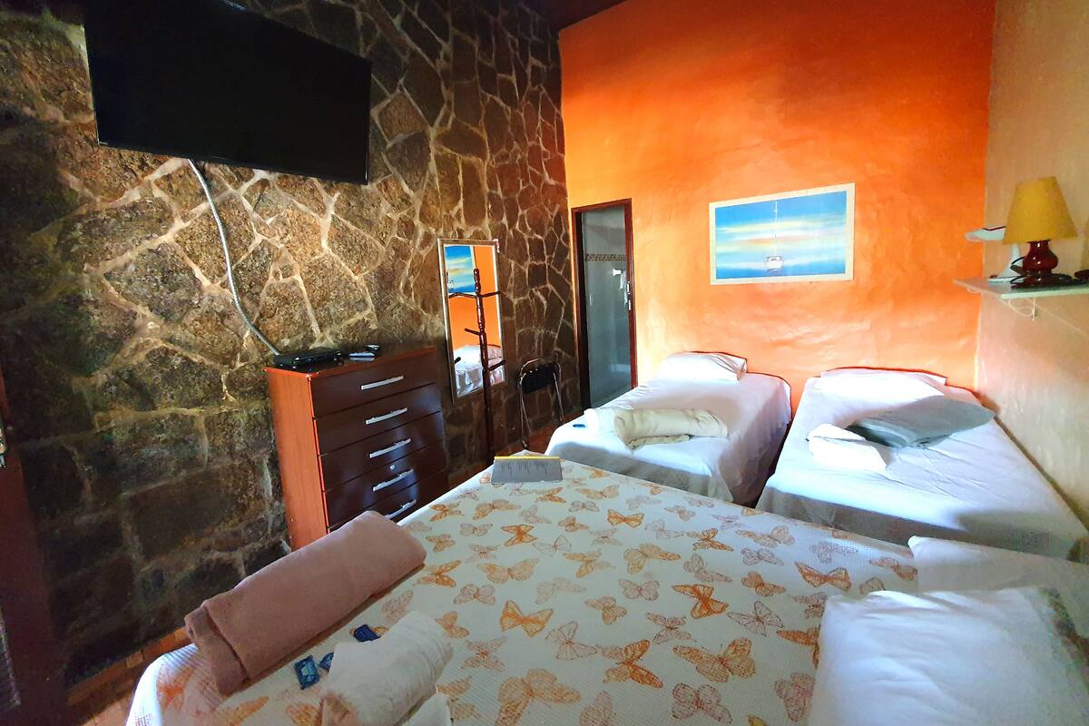 A hotel room with a stone wall, a bed with a butterfly-patterned bedspread, a bedside table with a lamp, and a painting of a boat on the wall.