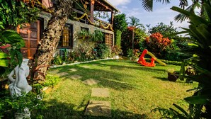 A lush garden with a stone pathway leading to a house with a wooden porch. - Suites Casa do Barão (Búzios)