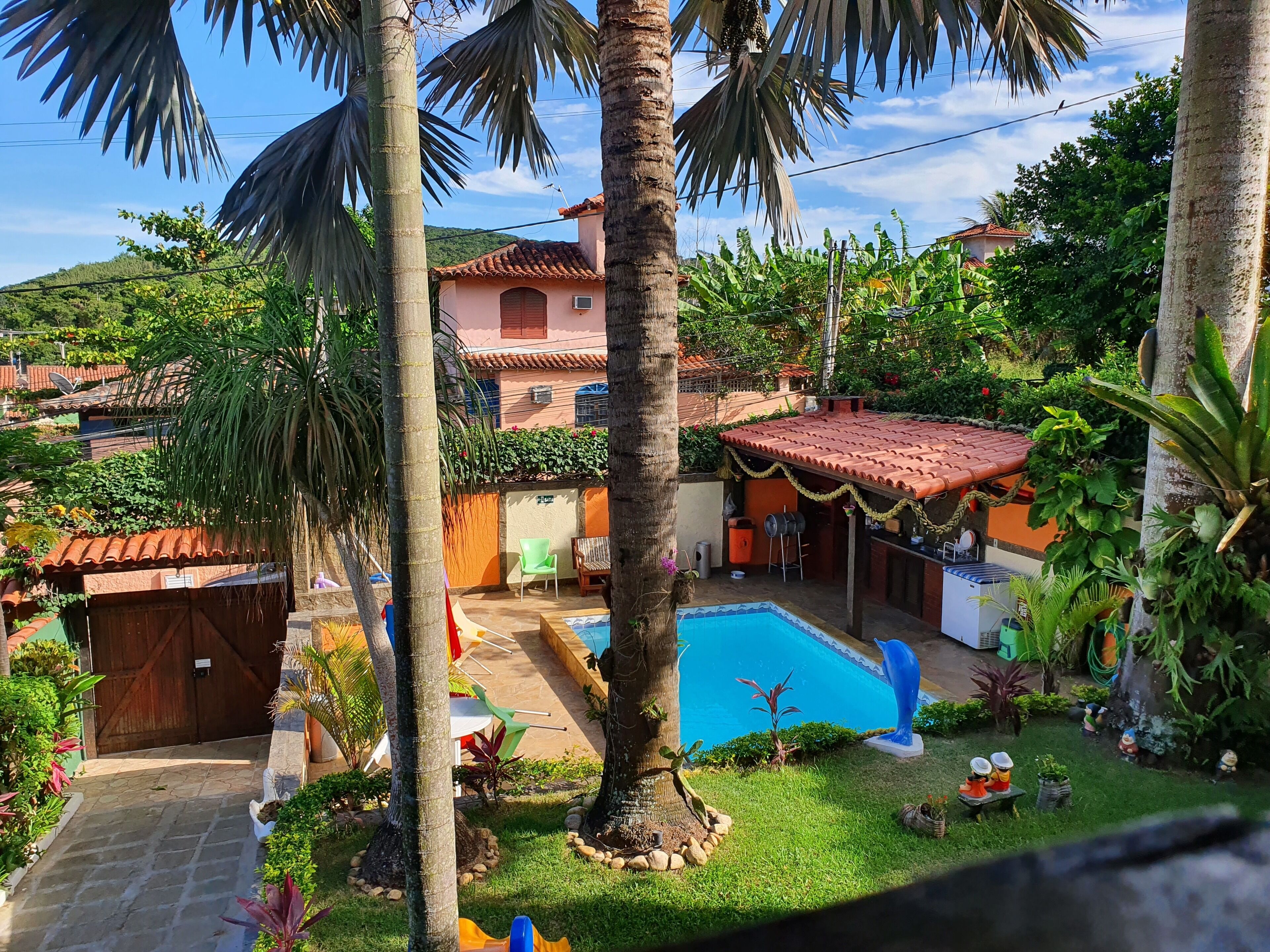 A pool area with a tiled deck, surrounded by palm trees and various plants.