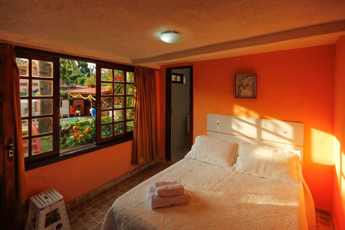 A hotel room with a large window, a bed with white linens, and a view of the outside.