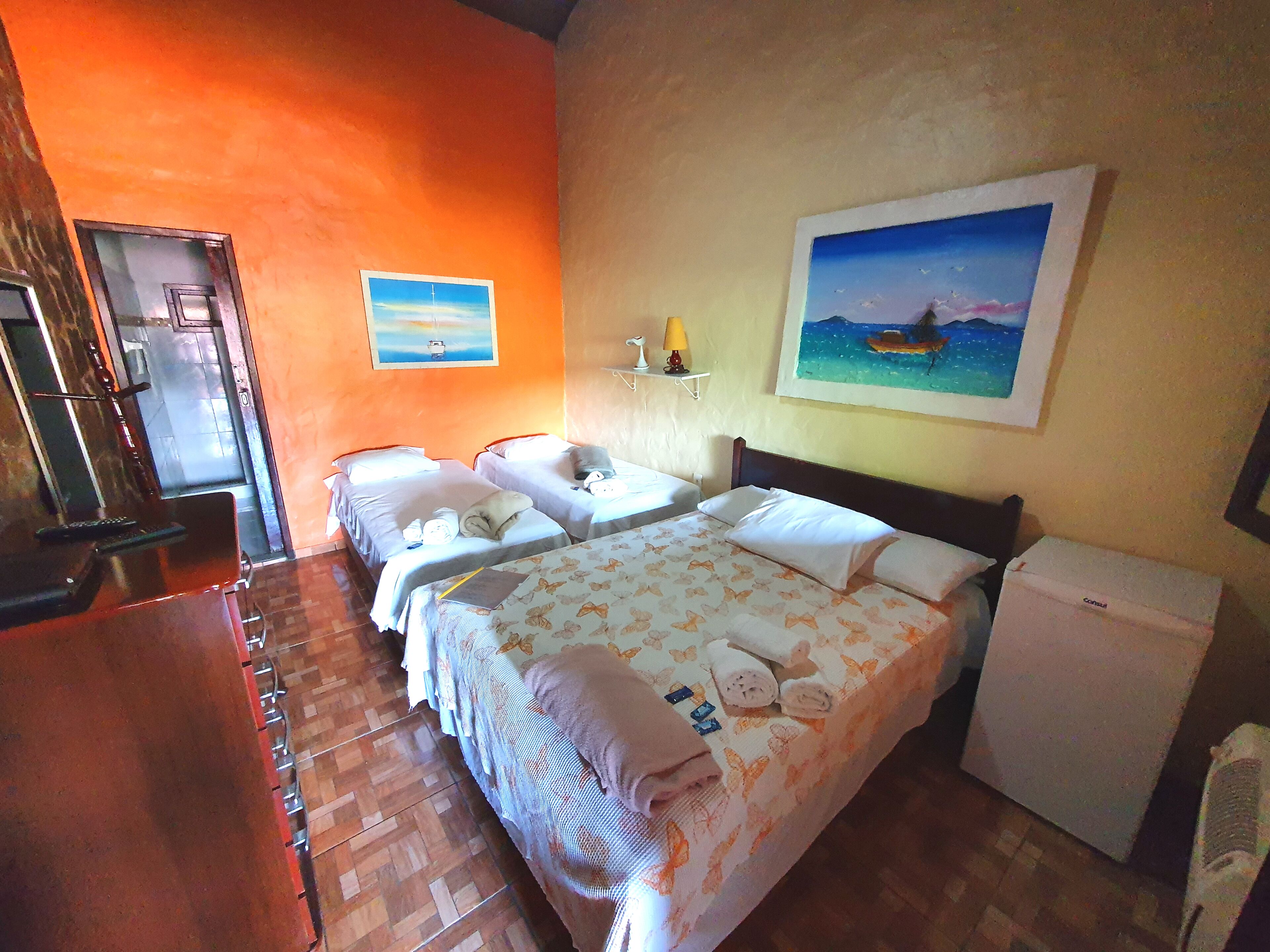A hotel room with two beds, a small refrigerator, a desk with a chair, and a window.
