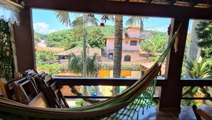 A hammock in a room with a view of a hillside and buildings. - Suites Casa do Barão (Búzios)