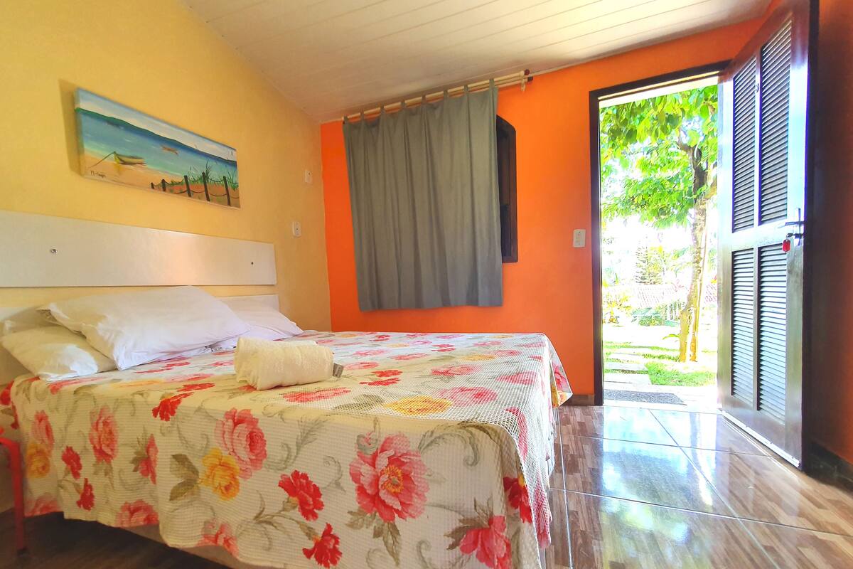 A bedroom with a bed, a painting, a window with curtains, and a door leading outside.