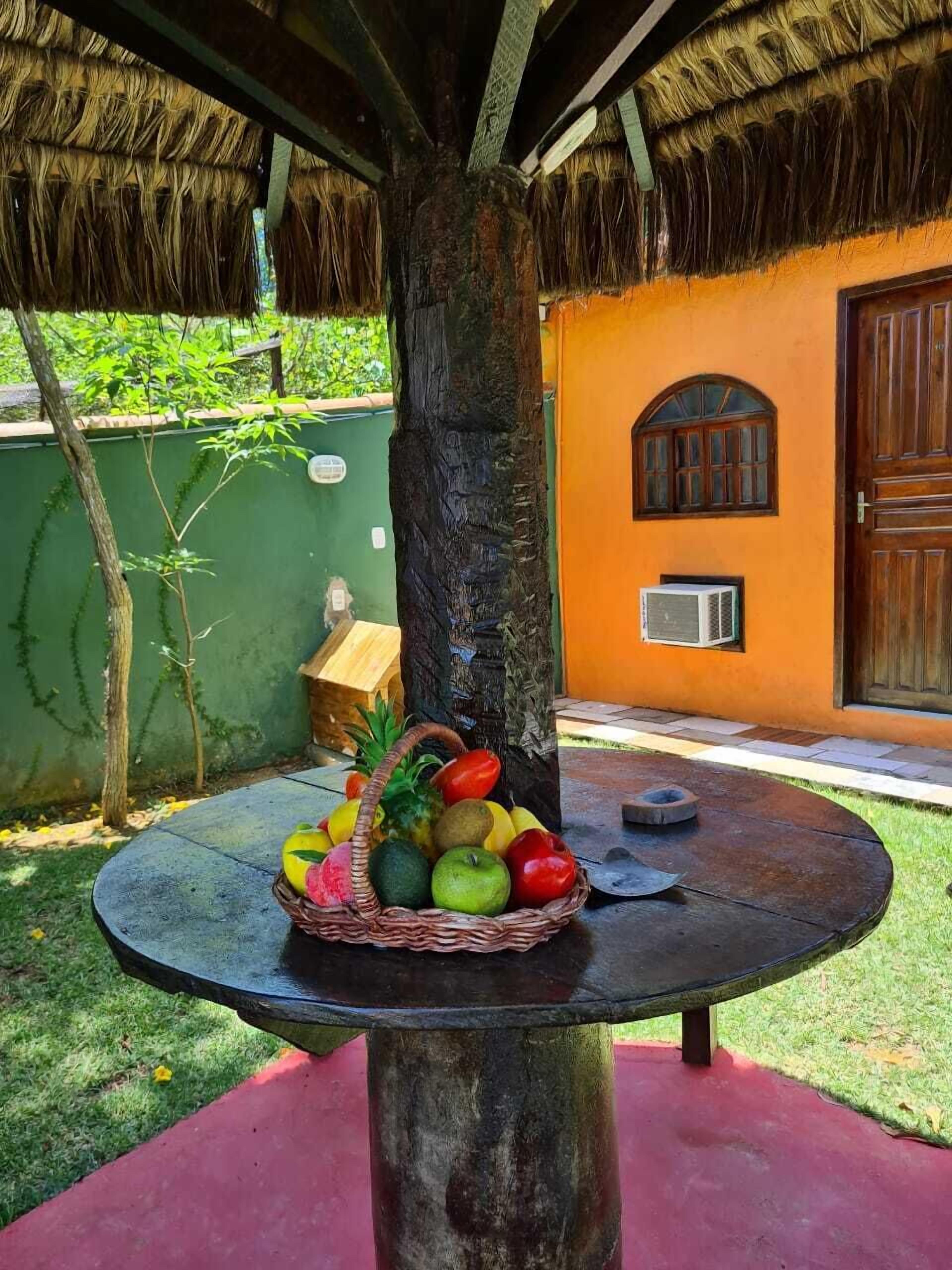 Un espace extérieur de style tropical, avec une table ronde placée sous un toit de chaume, entourée d’un mur végétal et d’une porte en bois.