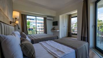 Habitación de hotel con dos camas, televisión y balcón con vistas a edificios y palmeras.