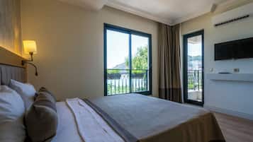A hotel room with a large bed, a TV mounted on the wall, and a balcony with a view.