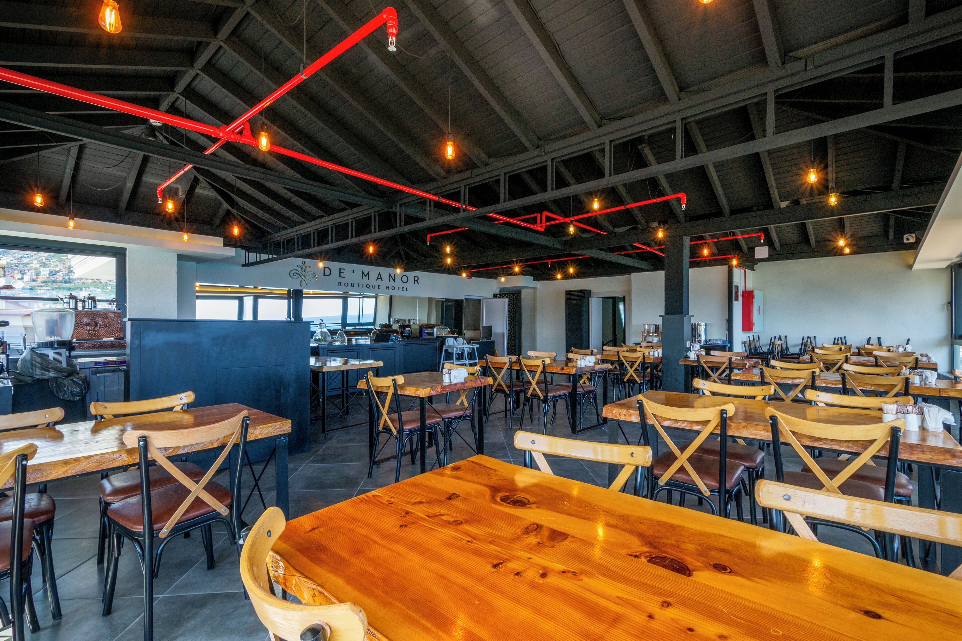 A spacious restaurant with wooden tables and chairs, a high ceiling with exposed beams, and a view of the city.