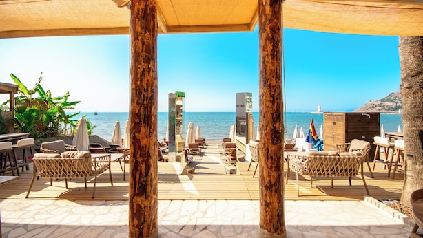 Eine Terrasse am Strand mit Holzmöbeln, Sonnenschirmen und Blick aufs Meer.