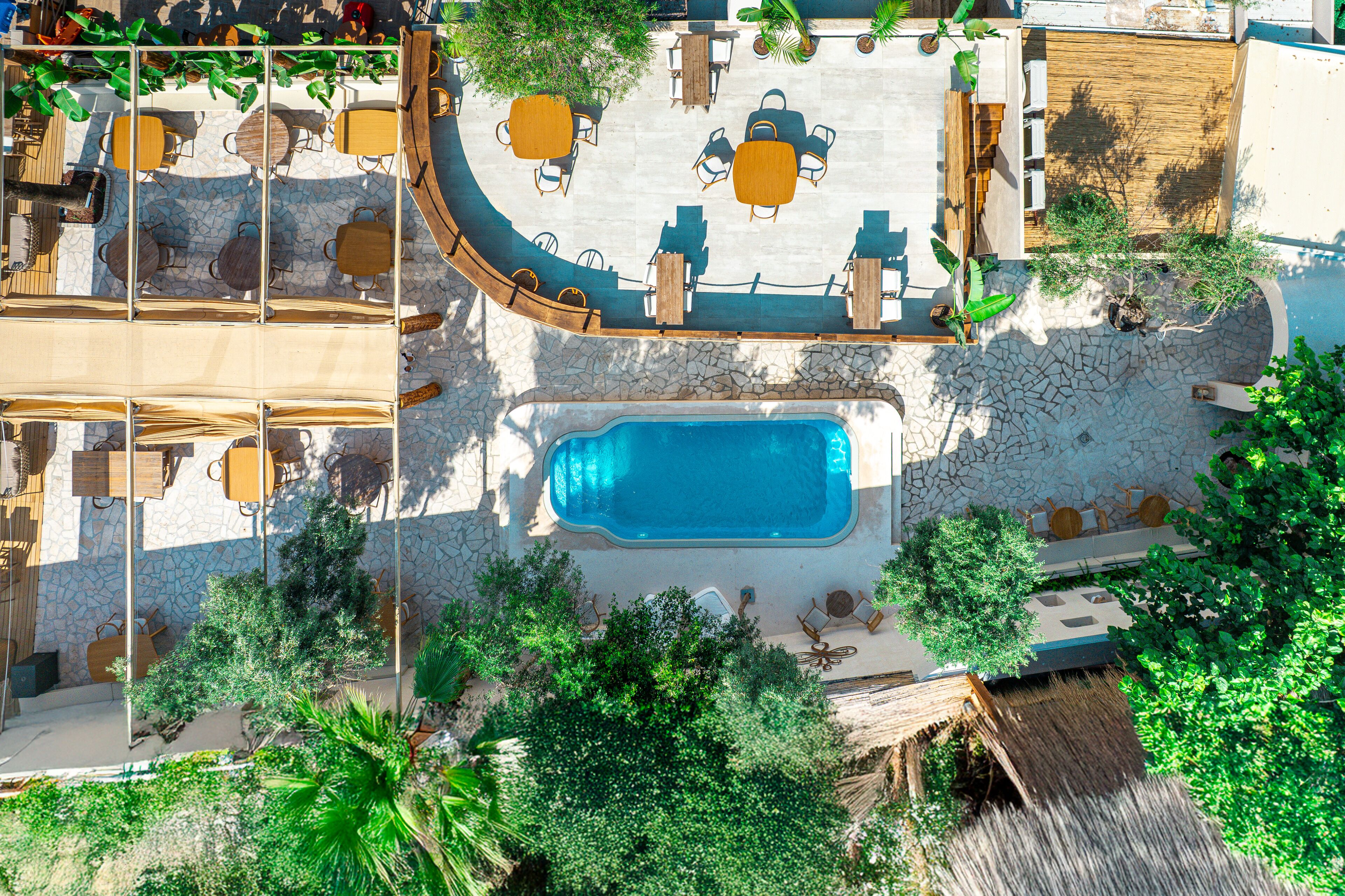 An aerial view of a resort with a swimming pool, outdoor seating areas, and lush greenery.