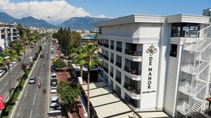 A multi-story hotel with balconies, a clear view of the street, and mountains in the background. - De Manor Hotel (Alanya)