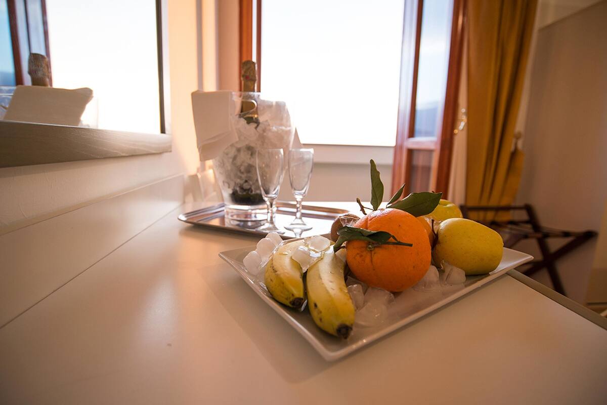 A tray with bananas, an orange, and a lemon on a white table with a window in the background.