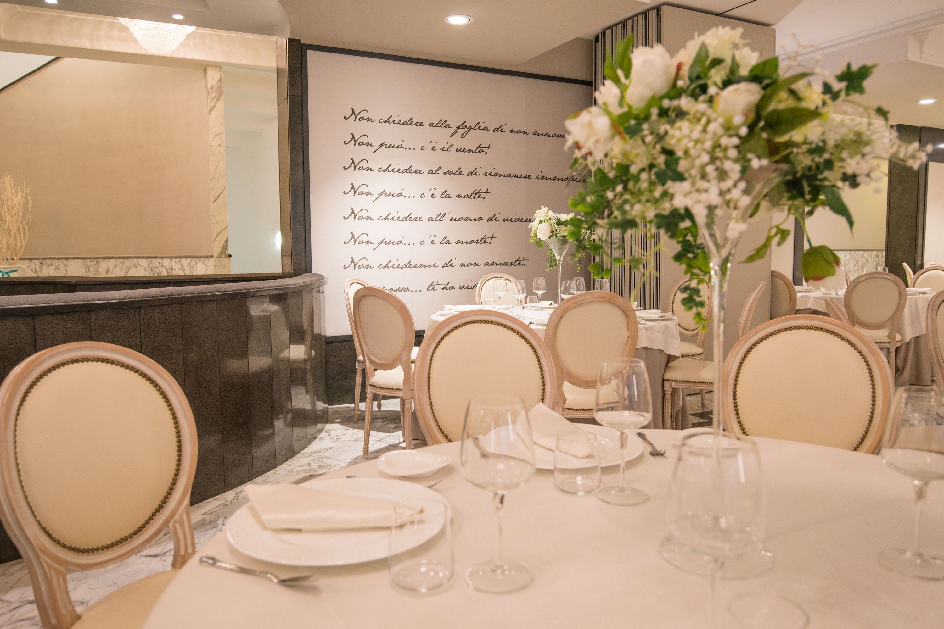A dining area with round tables set for a meal, chairs, and a floral centerpiece.