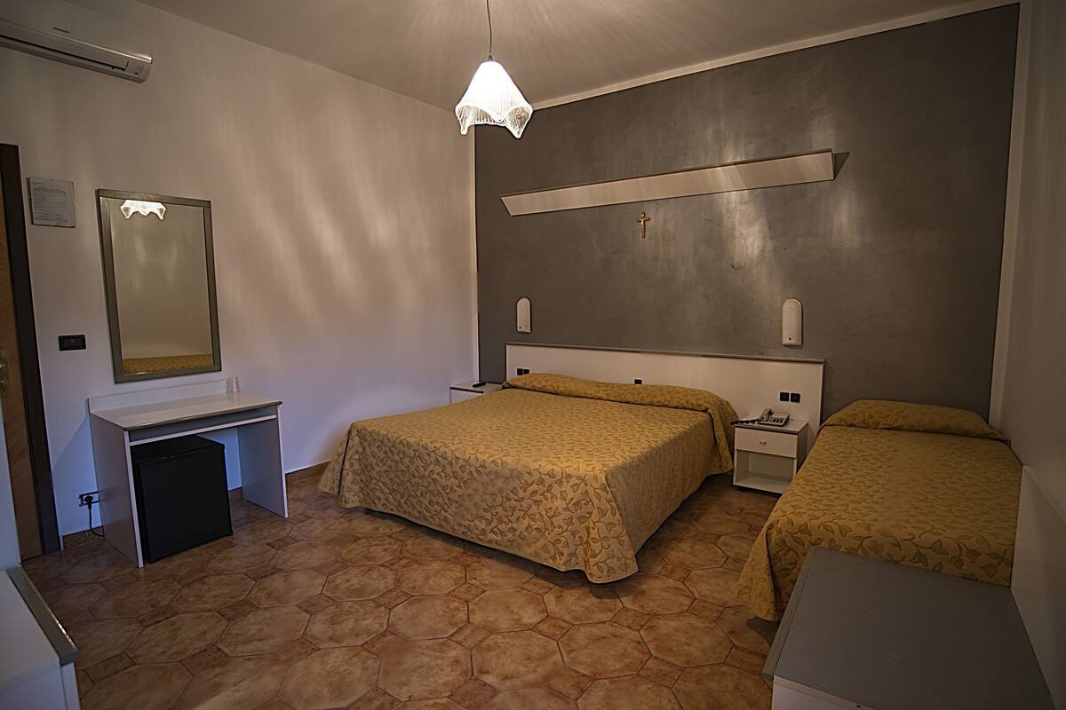 A hotel room with a bed, bedside table, desk, and a mirror.