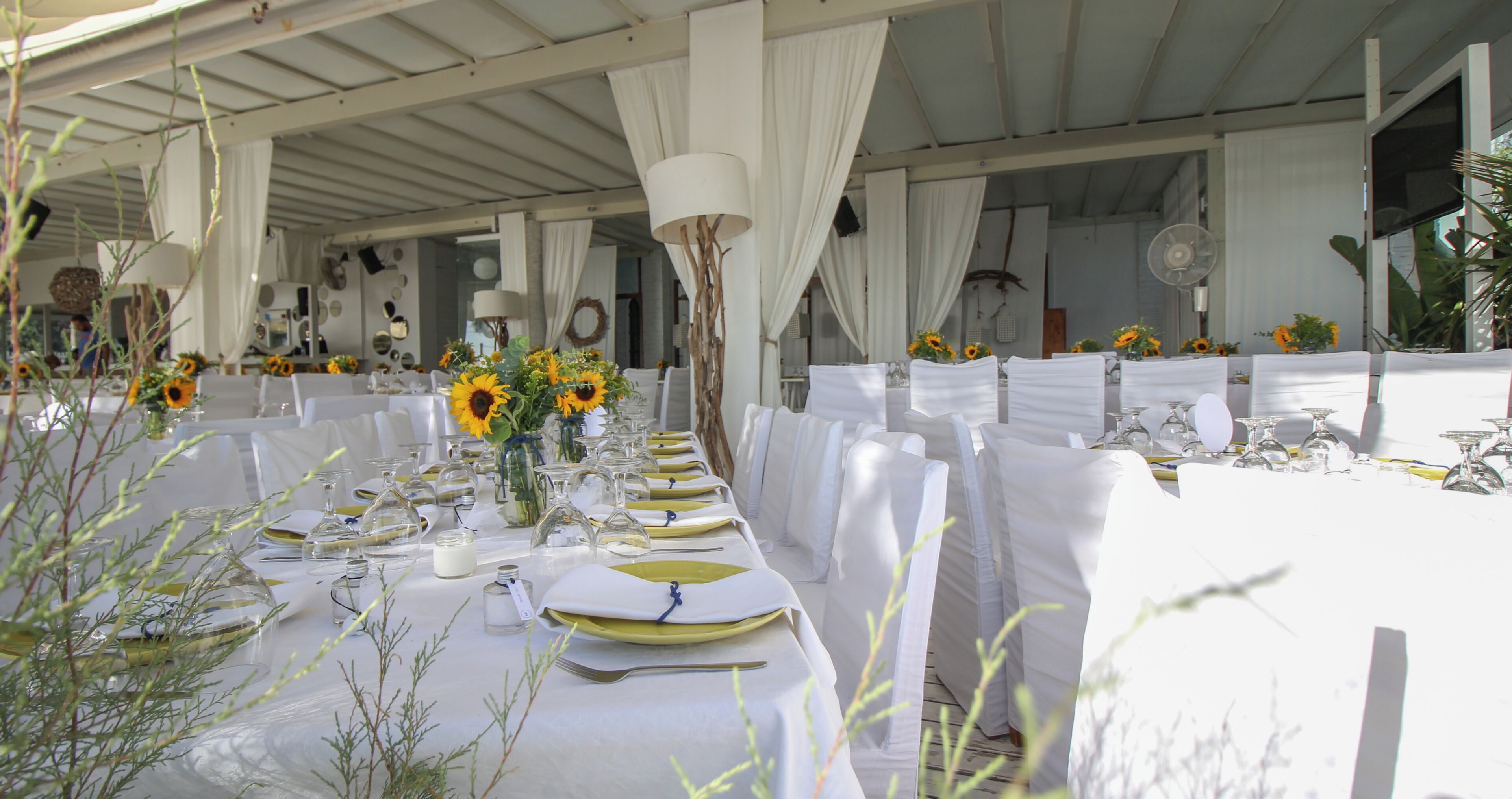 A long dining table with white tablecloths, sunflowers, and clear glassware.