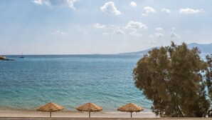 Une plage avec une eau d’un bleu limpide, quelques parasols en paille et un arbre.