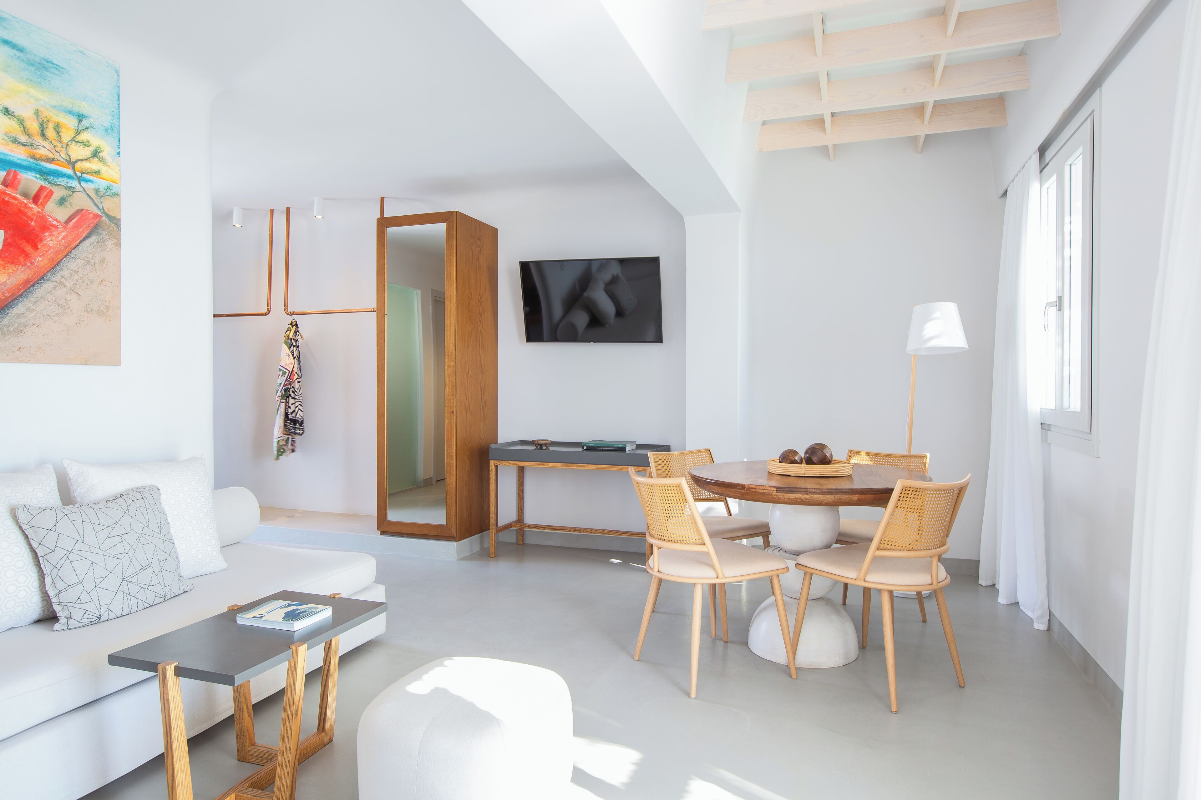 Una sala moderna con sofá, mesa de centro, mesa de comedor con sillas, televisor montado en la pared y un ventanal grande.