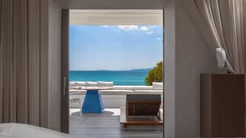 A room with a bed, a view of the sea, a blue chair, and a wooden cabinet.