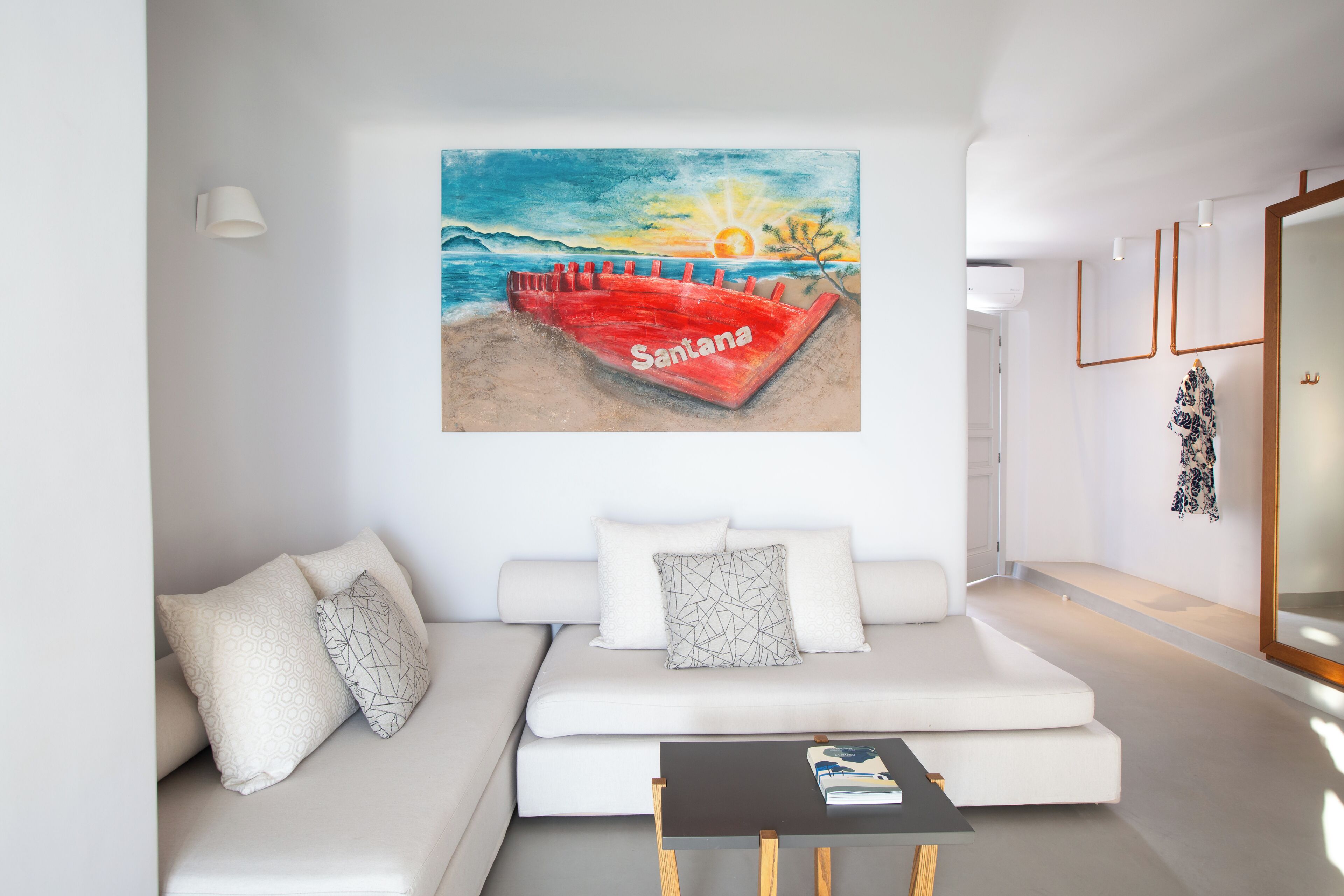 A modern living room with a white sofa, a coffee table, and a colorful beach painting on the wall.