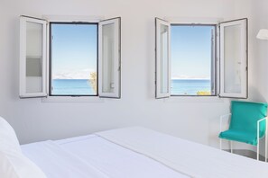 A room with a bed, two open windows with a view of the sea, and a teal chair. - Santana Beach (Naxos)
