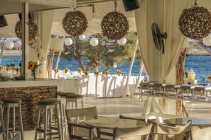 An outdoor dining area with round tables and chairs, white drapes, and decorative wicker balls.