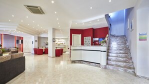 A spacious lobby with a marble floor, a reception desk, and a staircase leading to upper floors.