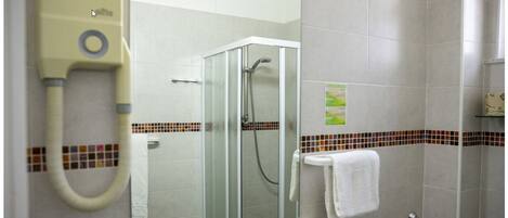 A bathroom with a glass shower enclosure, a hairdryer, a glass sink, and a towel rack.