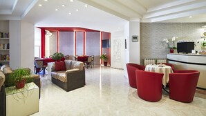 A modern hotel lobby with a seating area, a reception desk, and a dining space.