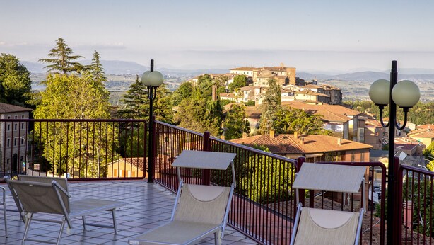 A terrace with two sun loungers, a metal railing, and a view of a town with buildings and trees.