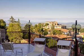 Una terraza con dos tumbonas, una barandilla de metal y vistas a un pueblo con edificios y árboles.