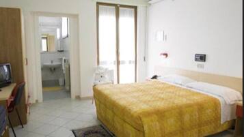 Habitación de hotel con cama, escritorio con silla, televisión y baño visible a través de una puerta abierta.