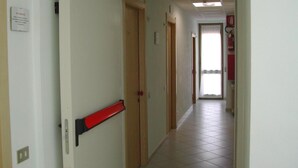 A hallway with a red fire alarm, a door, and a window at the end.
