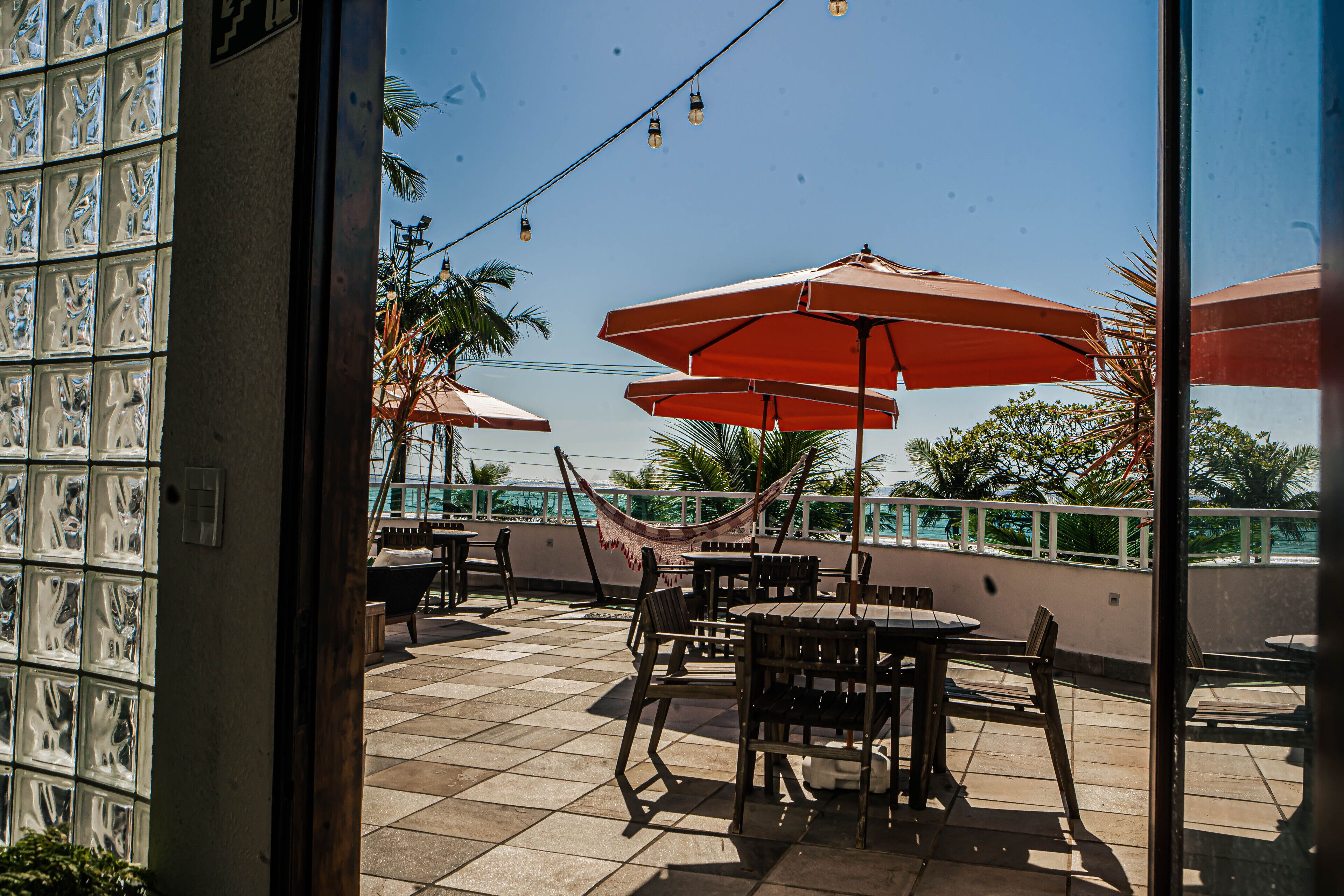 An outdoor patio with tiled flooring, wooden tables and chairs, and red umbrellas.
