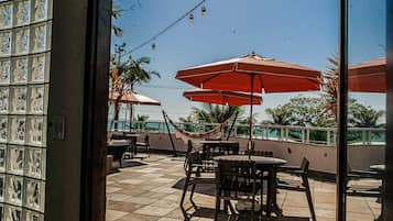 An outdoor patio with tiled flooring, wooden tables and chairs, and red umbrellas.