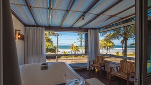 Una habitación con un ventanal grande que da a una playa, una terraza de madera y un jacuzzi.