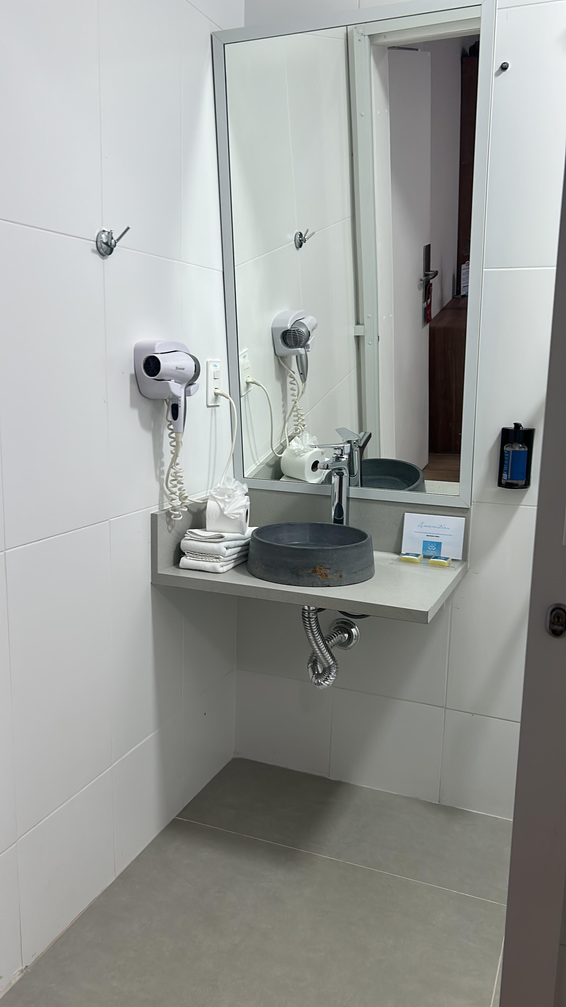 A bathroom with a sink, mirror, towel dispenser, and hairdryer.
